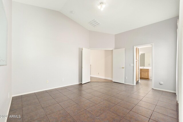 unfurnished bedroom with dark tile patterned floors, lofted ceiling, and ensuite bathroom