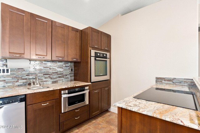 kitchen with appliances with stainless steel finishes, decorative backsplash, sink, and light stone counters