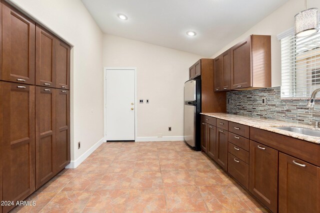 kitchen featuring stainless steel fridge, decorative backsplash, vaulted ceiling, light stone countertops, and sink