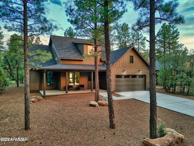 view of front facade featuring a porch, an attached garage, a shingled roof, concrete driveway, and board and batten siding