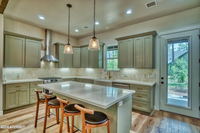 kitchen with hanging light fixtures, wall chimney exhaust hood, a center island, light wood-type flooring, and tasteful backsplash