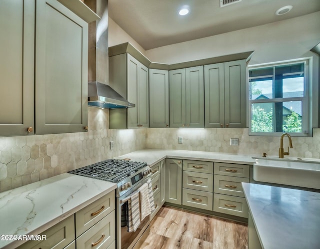 kitchen featuring tasteful backsplash, light hardwood / wood-style floors, light stone counters, wall chimney exhaust hood, and stainless steel range