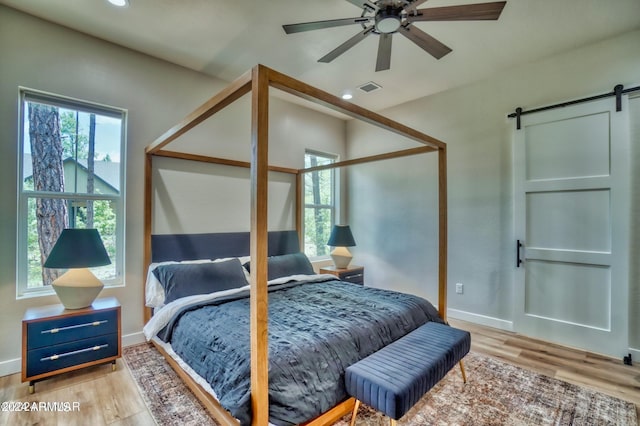 bedroom with ceiling fan, a barn door, multiple windows, and light hardwood / wood-style floors