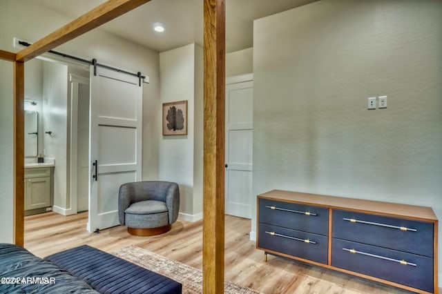 bedroom featuring a barn door, light wood-type flooring, and connected bathroom