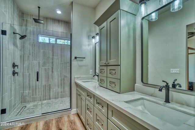 bathroom featuring dual bowl vanity, hardwood / wood-style flooring, and a shower with door