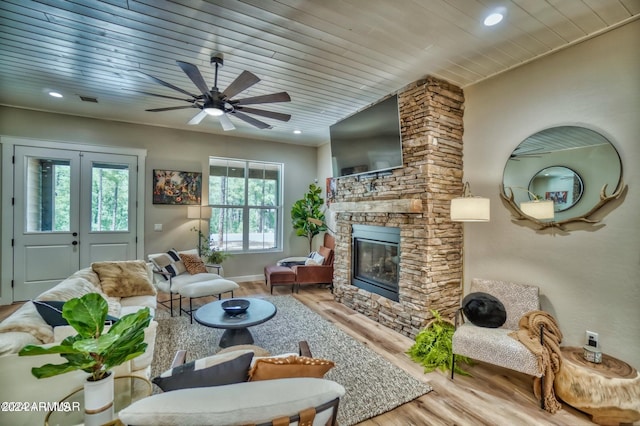 living room featuring a stone fireplace, light wood-type flooring, ceiling fan, and a wealth of natural light