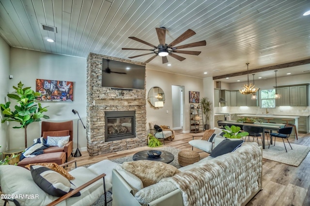 living room with light wood-type flooring, ceiling fan with notable chandelier, a stone fireplace, and wood ceiling