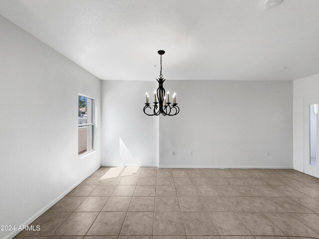 empty room with light tile patterned flooring and an inviting chandelier