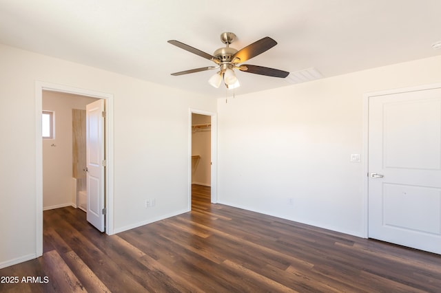 unfurnished bedroom featuring ceiling fan, a closet, dark hardwood / wood-style flooring, and a walk in closet