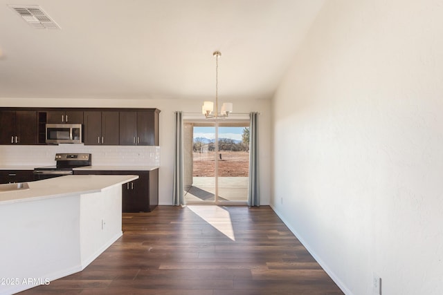 kitchen featuring appliances with stainless steel finishes, a chandelier, hanging light fixtures, dark brown cabinetry, and dark wood-type flooring