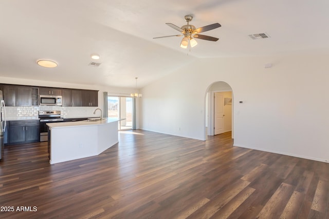 kitchen featuring appliances with stainless steel finishes, a kitchen island with sink, dark brown cabinets, backsplash, and vaulted ceiling