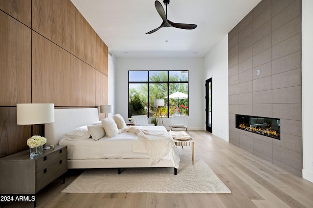 bedroom with a tile fireplace, baseboards, ceiling fan, and light wood finished floors