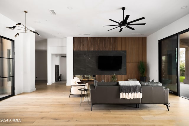 living room featuring light wood-type flooring, wooden walls, visible vents, and a ceiling fan