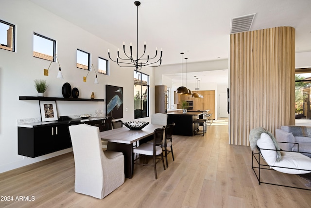 dining area with light wood-style flooring, a towering ceiling, visible vents, and an inviting chandelier