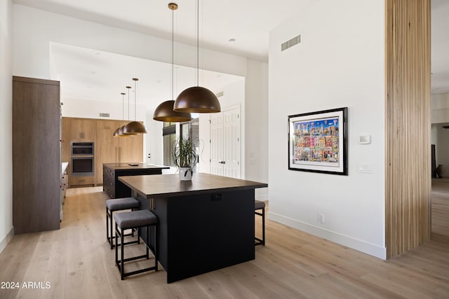 kitchen with a kitchen bar, a center island, light hardwood / wood-style floors, and hanging light fixtures