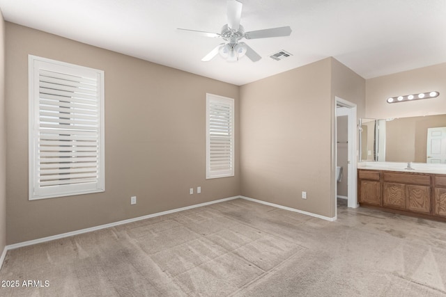 unfurnished bedroom with sink, ensuite bath, light colored carpet, and ceiling fan