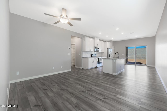 interior space with hardwood / wood-style floors, white cabinets, a center island with sink, and stainless steel appliances