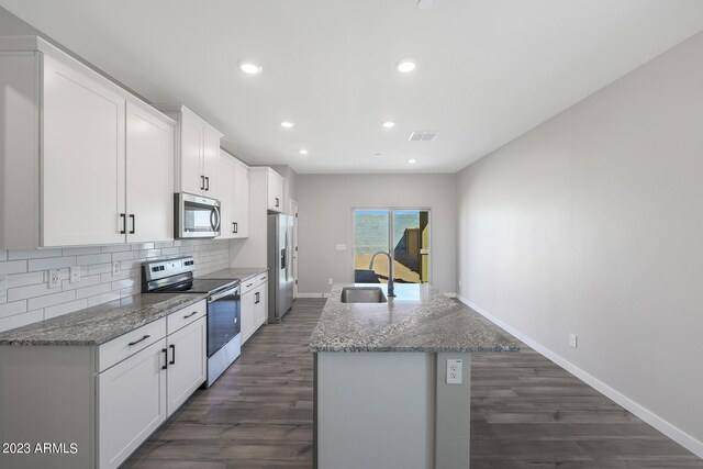 kitchen featuring stainless steel appliances, an island with sink, sink, light stone counters, and dark hardwood / wood-style floors