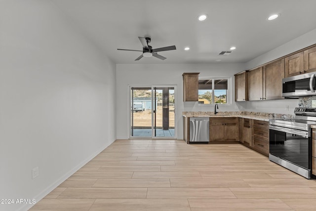 kitchen featuring sink, ceiling fan, light stone countertops, light wood-type flooring, and stainless steel appliances