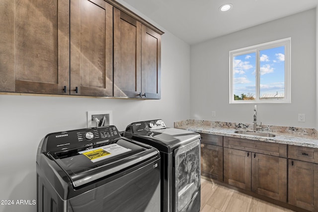 laundry room with cabinets, light hardwood / wood-style floors, washing machine and clothes dryer, and sink