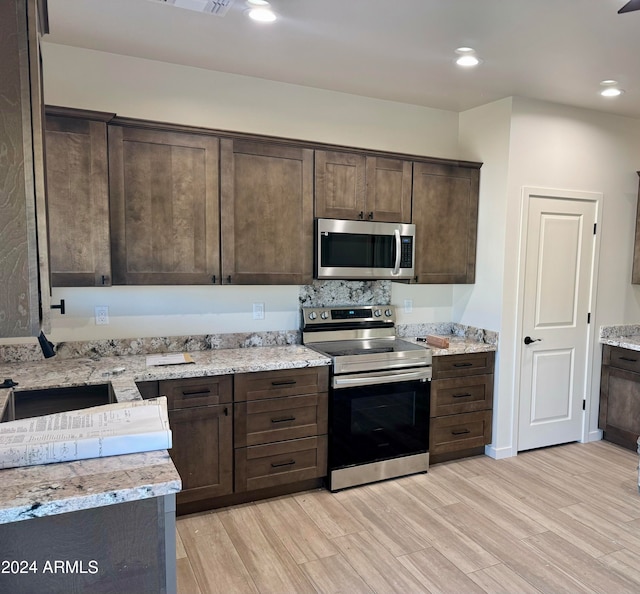 kitchen with dark brown cabinetry, light stone counters, stainless steel appliances, and light wood-type flooring