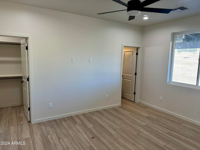 unfurnished bedroom featuring a closet, a walk in closet, ceiling fan, and light hardwood / wood-style flooring