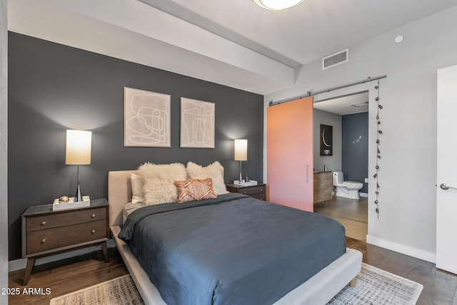 bedroom featuring connected bathroom, a barn door, and dark hardwood / wood-style flooring