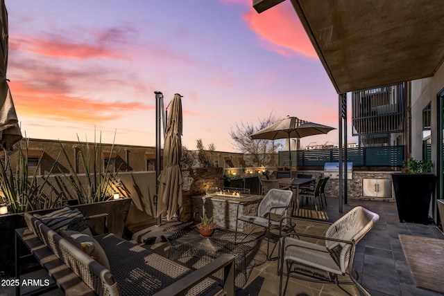 patio terrace at dusk featuring an outdoor kitchen and a grill