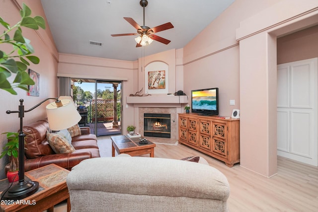 living room featuring a ceiling fan, a fireplace, visible vents, and light wood-style floors