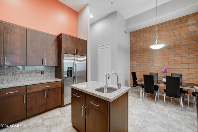 kitchen featuring sink, hanging light fixtures, a high ceiling, brick wall, and stainless steel fridge