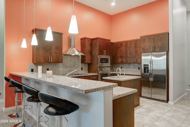 kitchen featuring kitchen peninsula, wall chimney exhaust hood, a breakfast bar, stainless steel appliances, and decorative light fixtures