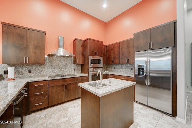 kitchen with sink, wall chimney exhaust hood, backsplash, an island with sink, and appliances with stainless steel finishes