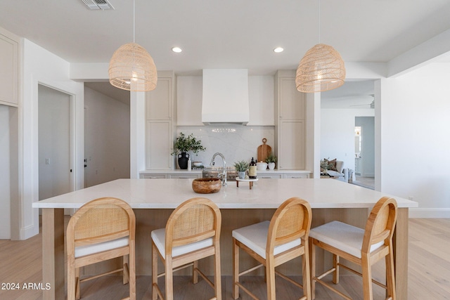 kitchen featuring a kitchen island with sink, backsplash, and decorative light fixtures