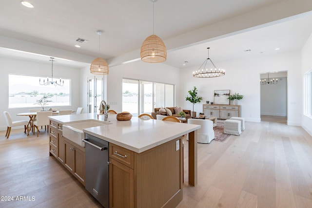 kitchen featuring pendant lighting, sink, a kitchen island with sink, stainless steel dishwasher, and light hardwood / wood-style flooring