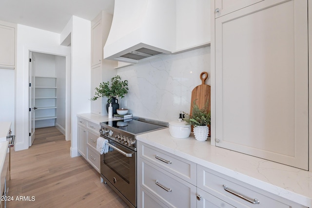 kitchen with tasteful backsplash, light stone counters, stainless steel range, custom range hood, and white cabinets