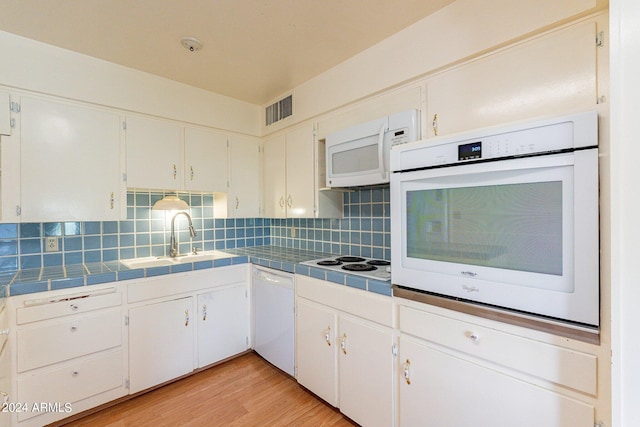 kitchen with white appliances, light hardwood / wood-style flooring, tile countertops, sink, and white cabinets