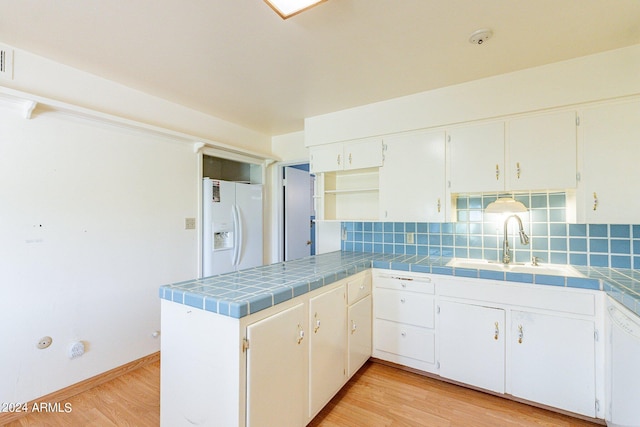 kitchen with white cabinets, white appliances, light hardwood / wood-style flooring, and tile counters