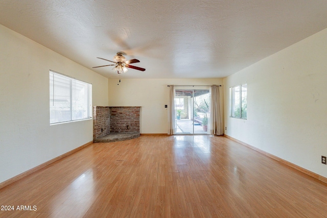 unfurnished living room with a healthy amount of sunlight, ceiling fan, a brick fireplace, and light hardwood / wood-style floors