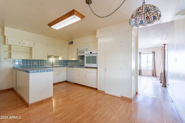 kitchen featuring white appliances, light hardwood / wood-style flooring, tile counters, sink, and white cabinetry