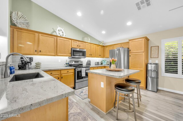46068 W Guilder Ave, Maricopa, AZ 85139 - kitchen with appliances with stainless steel finishes, vaulted ceiling, light stone counters, a center island, and decorative backsplash