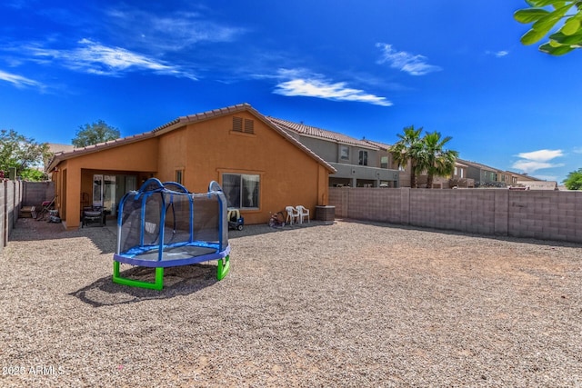36480 W El Greco St, Maricopa, AZ 85138 - rear view of property with a trampoline, a fenced backyard, central AC, a tiled roof, and stucco siding