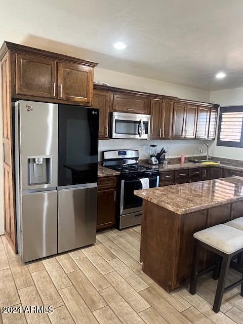 kitchen with a breakfast bar, dark brown cabinets, stainless steel appliances, and stone counters