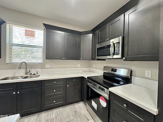 kitchen with light countertops, stainless steel appliances, dark cabinets, and a sink