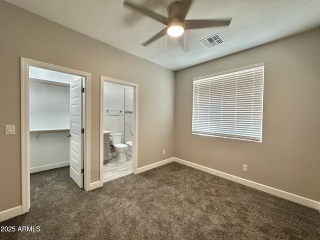 unfurnished bedroom with ensuite bath, visible vents, baseboards, a spacious closet, and dark carpet