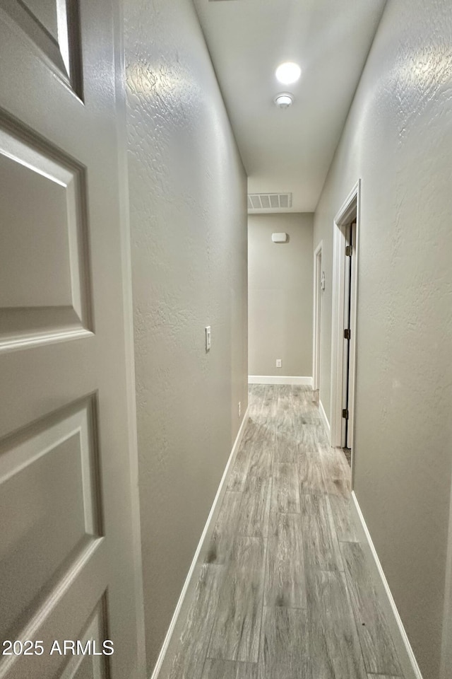 hall featuring baseboards, visible vents, a textured wall, and wood finished floors