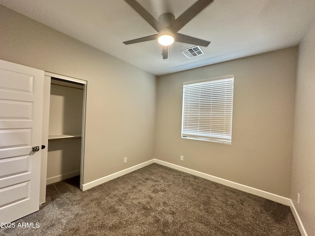 unfurnished bedroom with visible vents, a closet, baseboards, dark colored carpet, and a ceiling fan