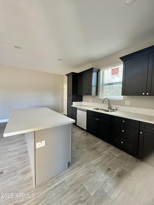 kitchen featuring stainless steel dishwasher, a center island, dark cabinetry, a sink, and light wood-style flooring