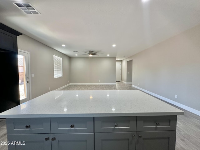 kitchen featuring gray cabinetry, light stone countertops, visible vents, and a center island