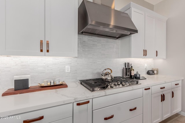 kitchen with white cabinetry, stainless steel gas stovetop, light stone countertops, and wall chimney exhaust hood