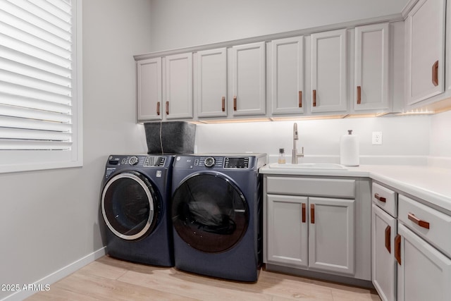 laundry area featuring cabinets, sink, washing machine and clothes dryer, and light hardwood / wood-style floors